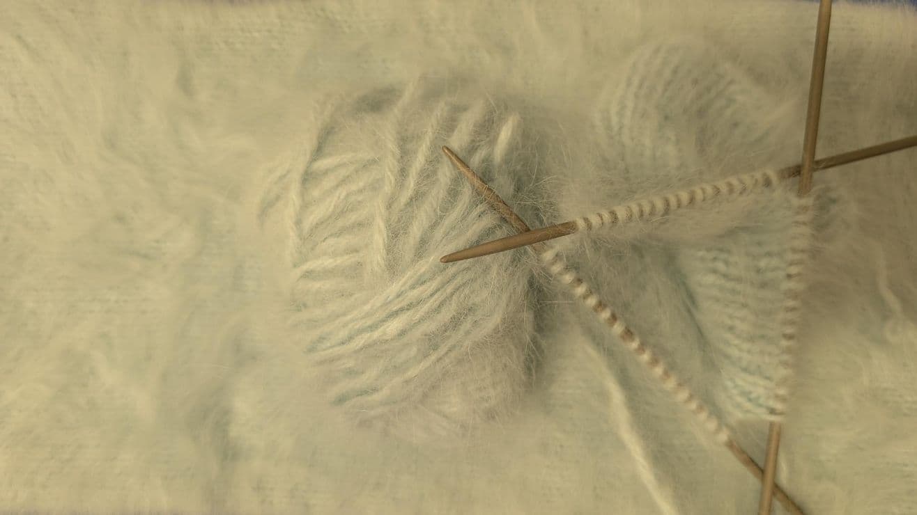 Ball of soft white wool with knitting needles