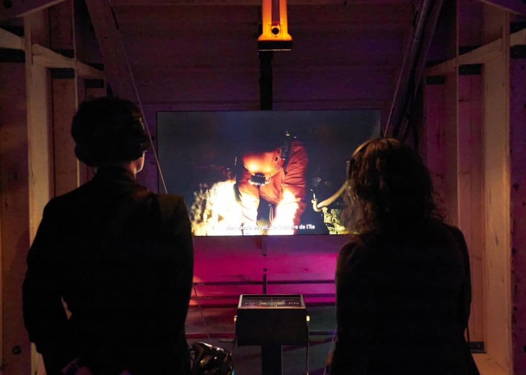 Two visitors watch a video in the exhibition Detours-Urban Experiences at the MEM.