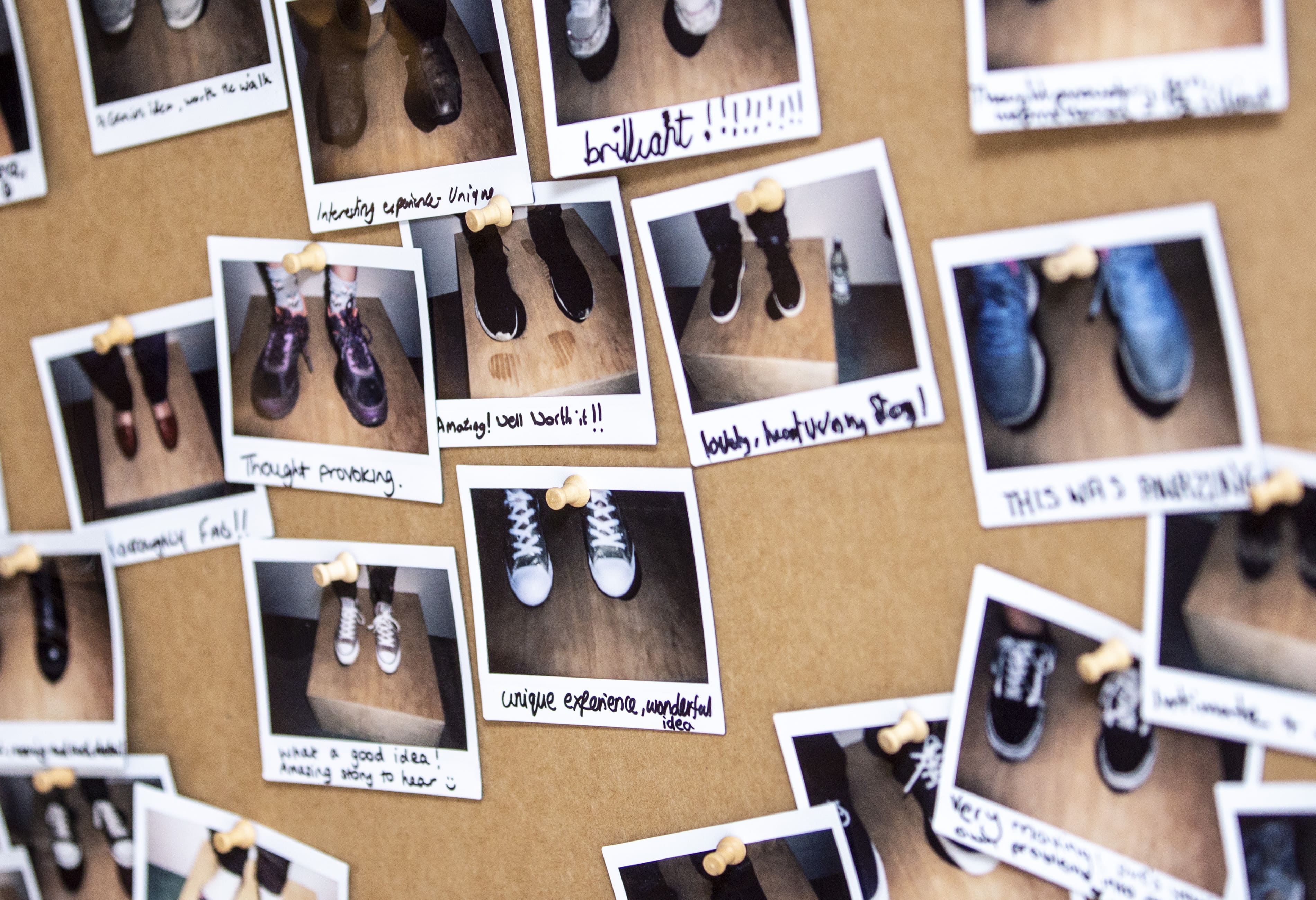 Polaroid pictures showing feet wearing a variety of shoes, displayed on a bulletin board.
