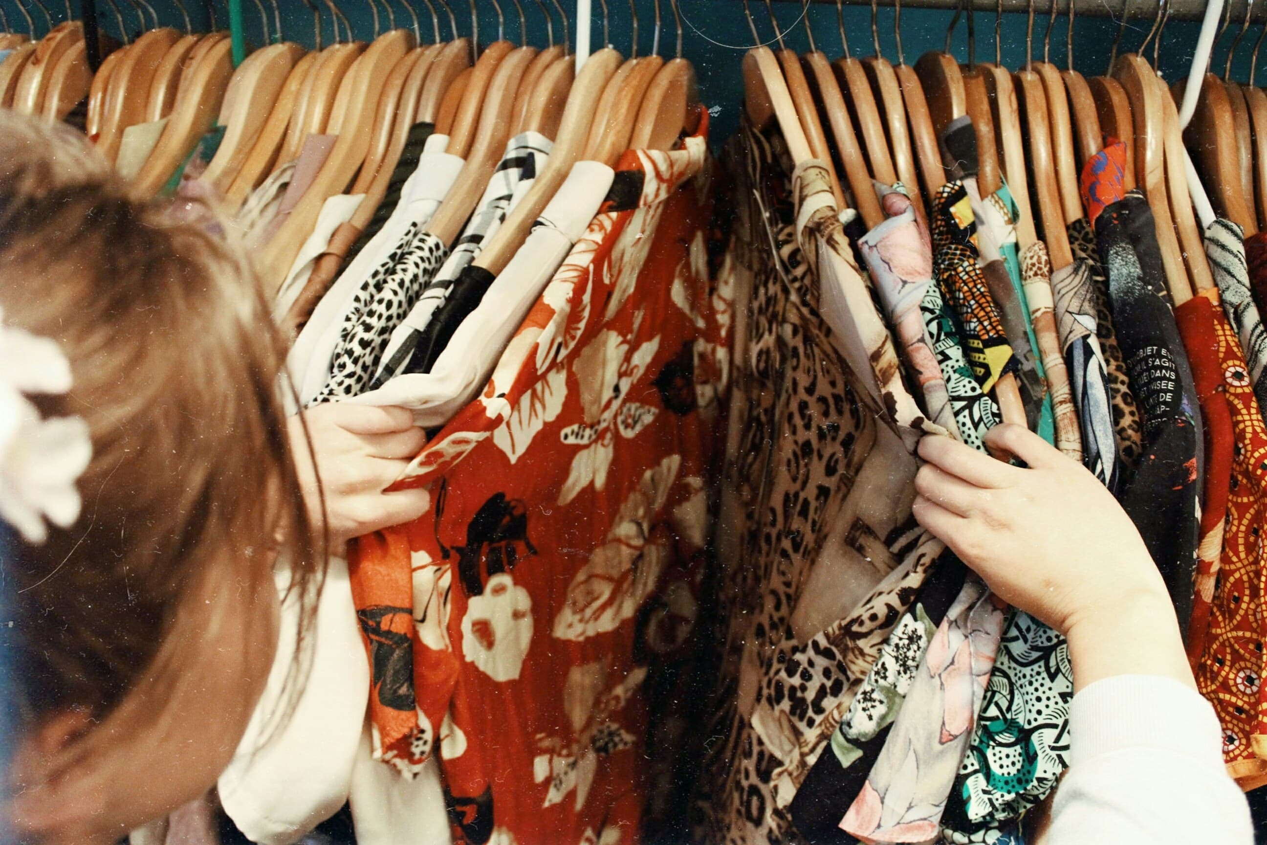 Person browsing a rack filled with colorful, patterned clothing hanging on wooden hangers.