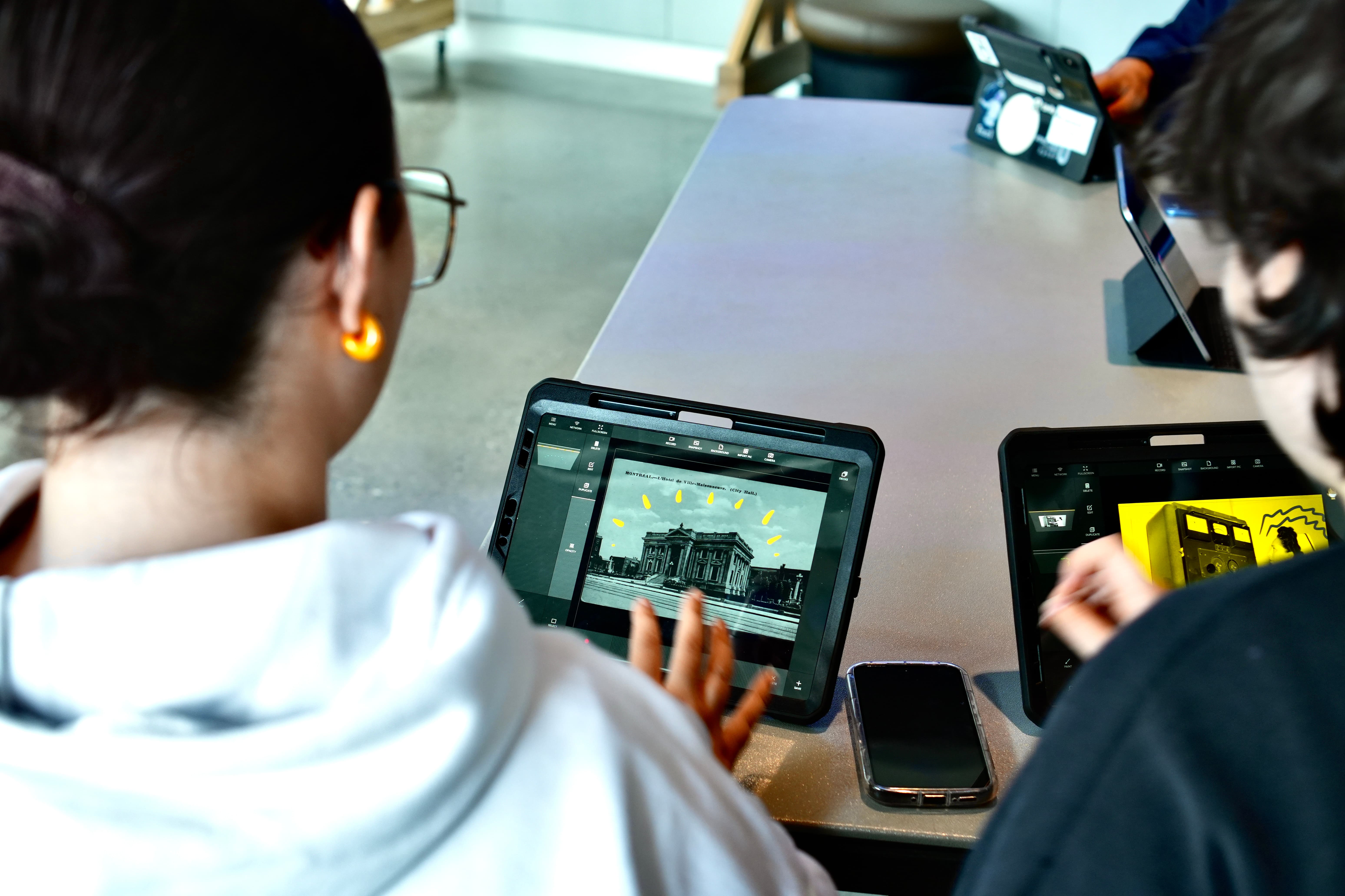 Deux adolescents en train d'utiliser des tablettes électroniques sur lesquels ont peut observer des image d'archives.
