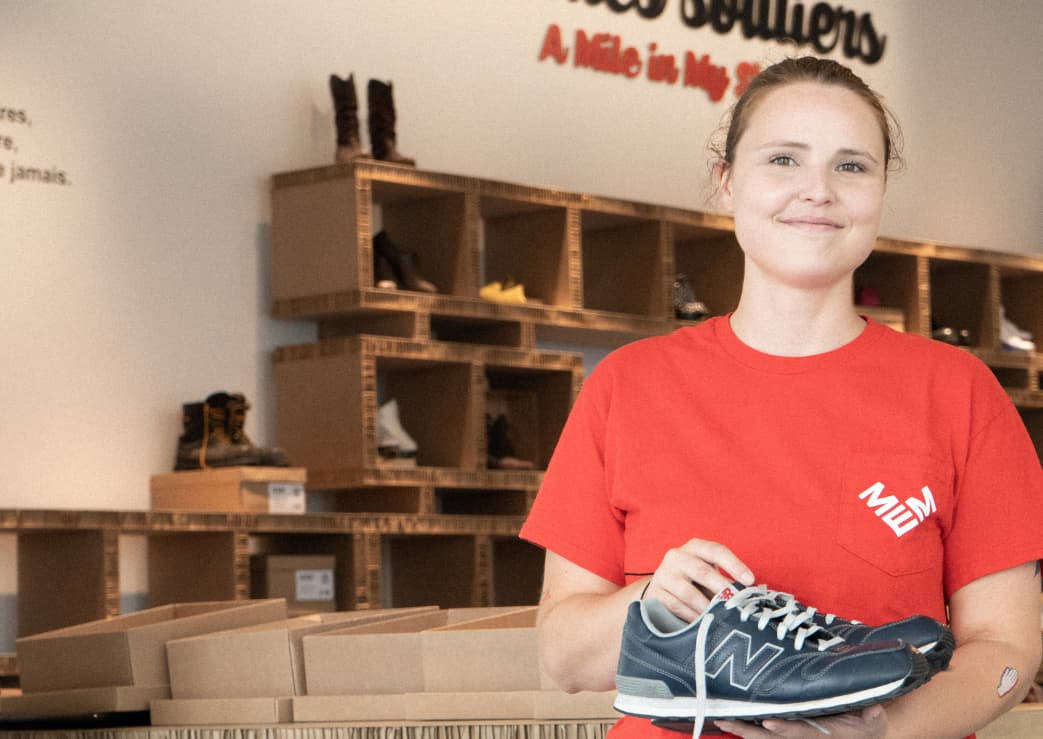 Photo d'une médiatrice du MEM avec une paire de chaussures dans les mains devant l'exposition