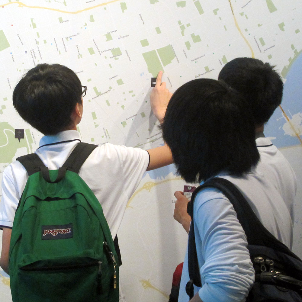 Three teenagers face a map of Montreal from behind. One of them points to a place.