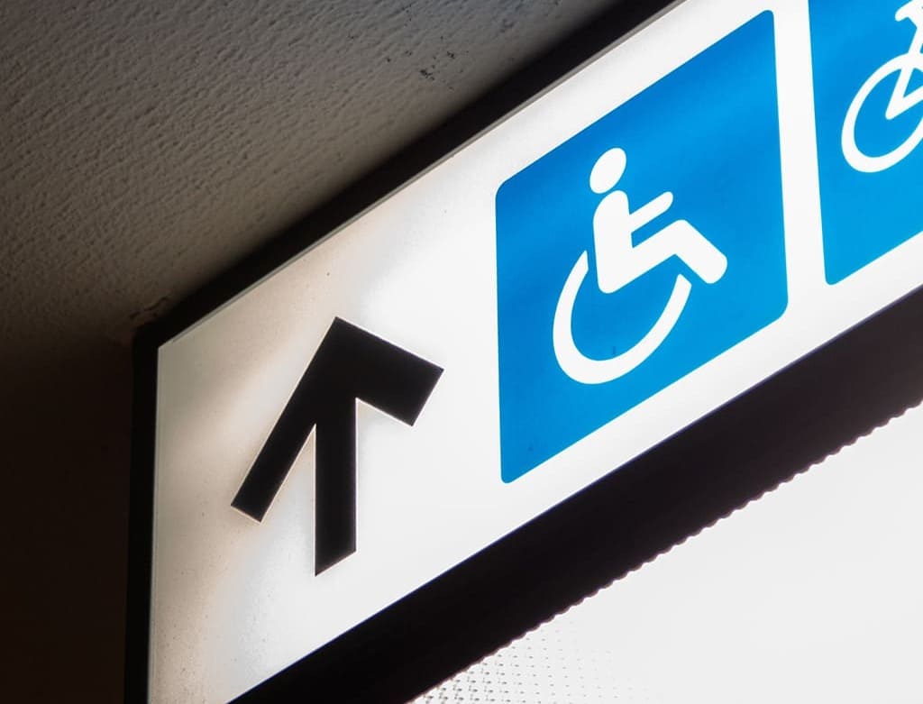 Gros plan sur un panneau de signalétique lumineux comprenant une flèche vers le haut et un pictogramme d’accessibilité en fauteuil roulant.