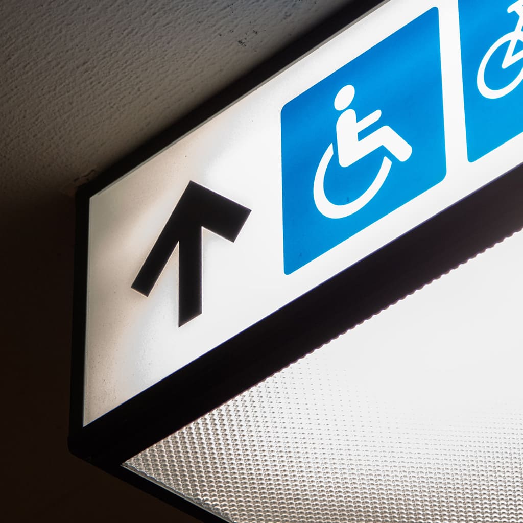 Close-up of a lighted sign with an upward arrow and a pictogram of wheelchair accessibility.
