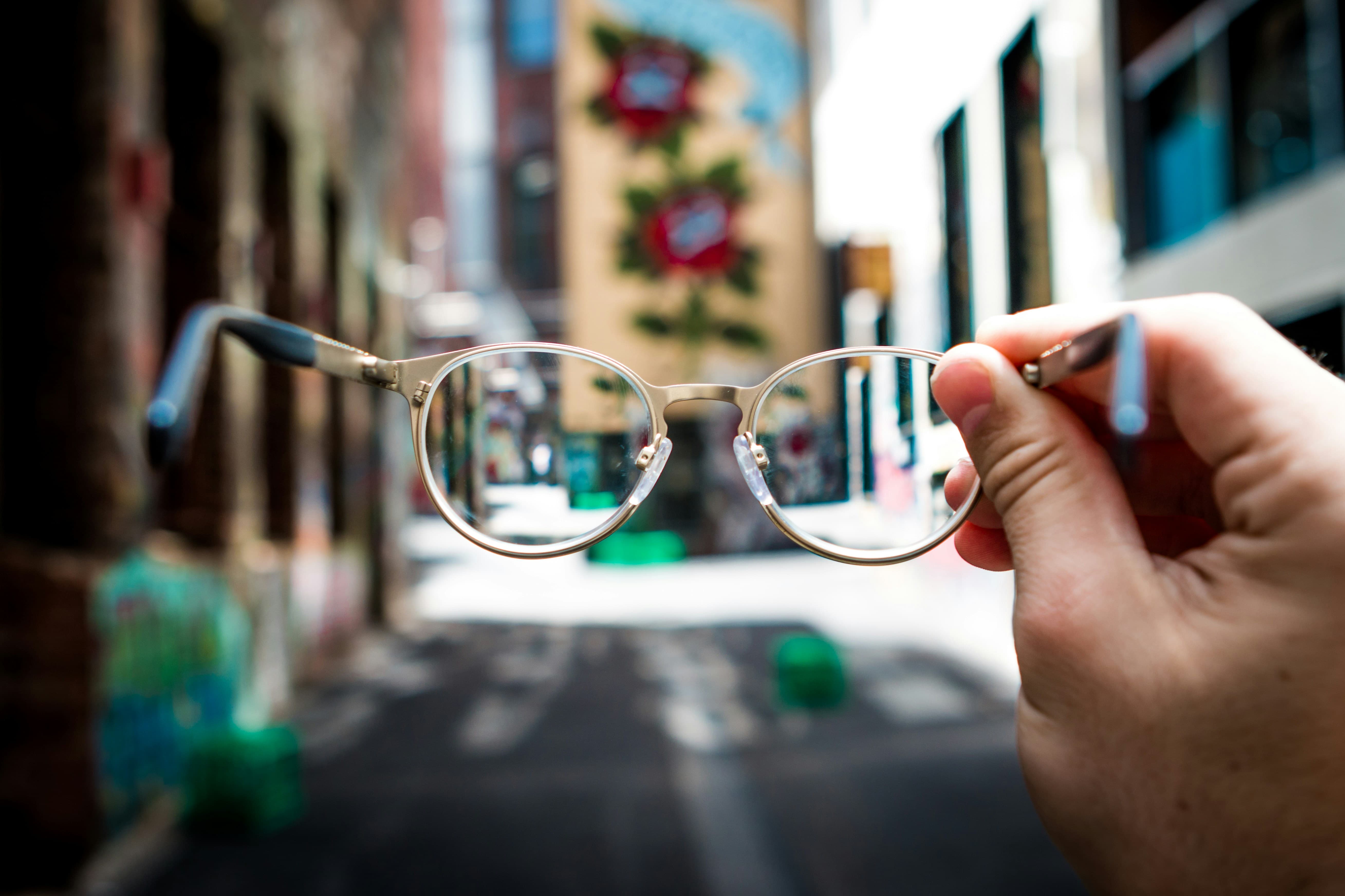 Main tenant des lunettes devant une vue urbaine floue.