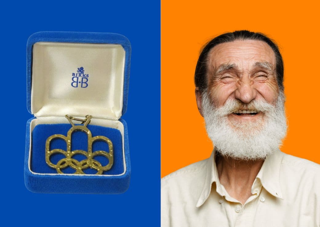 À gauche, un coffret bleu ouvert contenant une broche dorée en forme des anneaux olympiques. À droite, une personne portant une chemise beige sur fond orange vif.